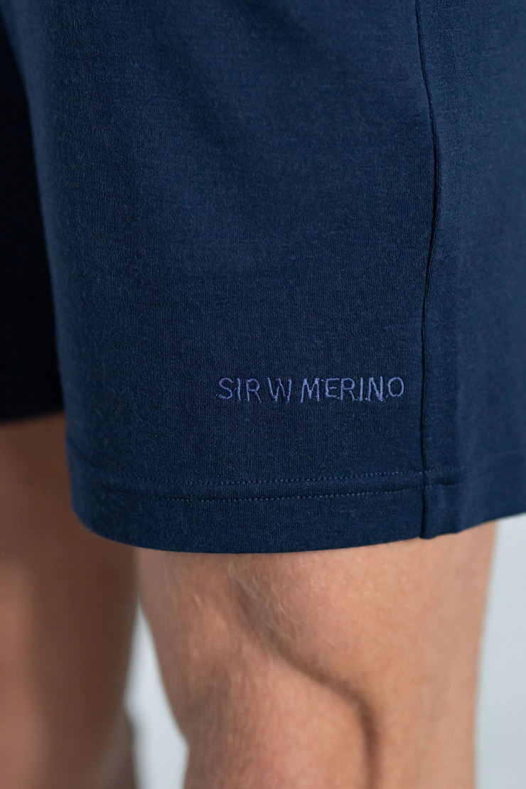 A person wearing navy blue merino wool lounge shorts and a white shirt.
