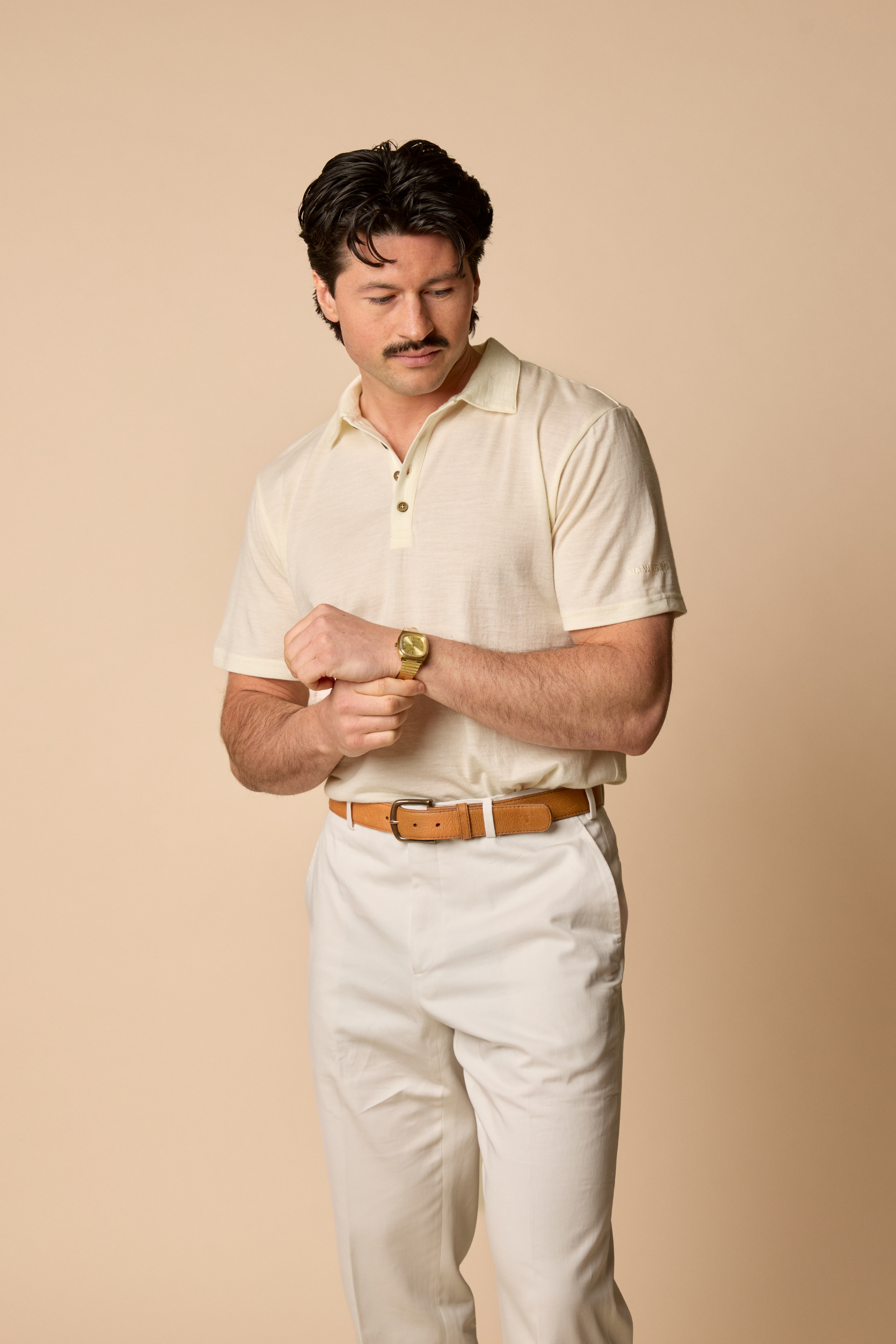 Man wearing a natural Sir W shirt and white pants with a brown belt against a beige background
