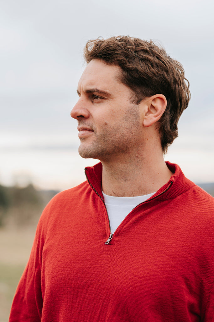 Man wearing a red Merino wool sweater and light blue jeans 