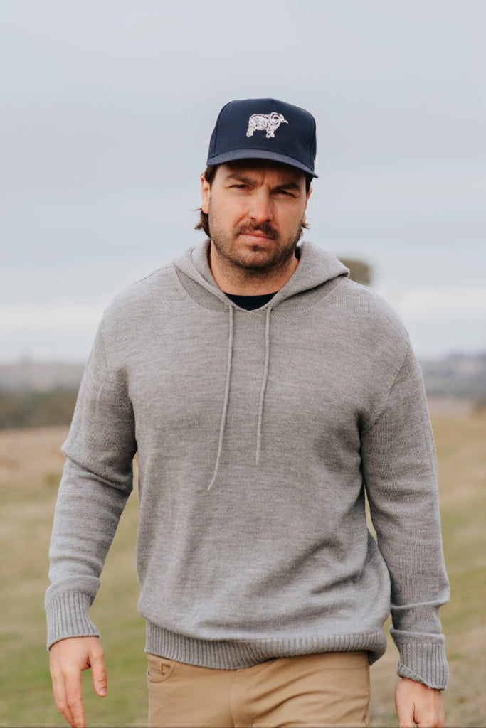Man wearing a gray merino hoodie and navy Sir W. cap with a logo outdoors