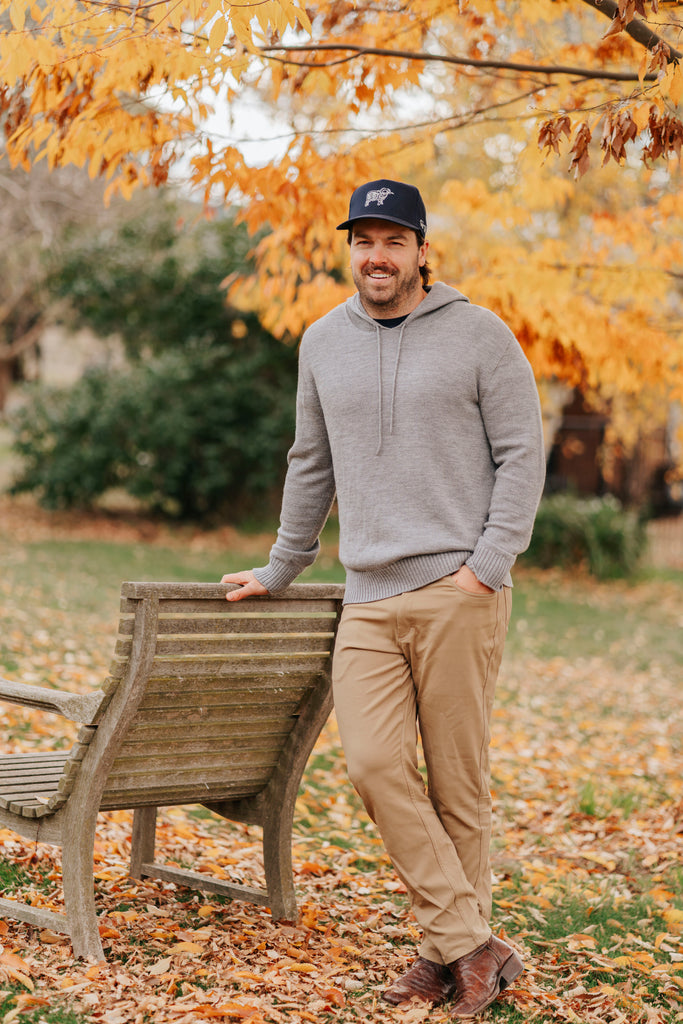 Man wearing a gray merino hoodie and navy Sir W. cap with a logo outdoors