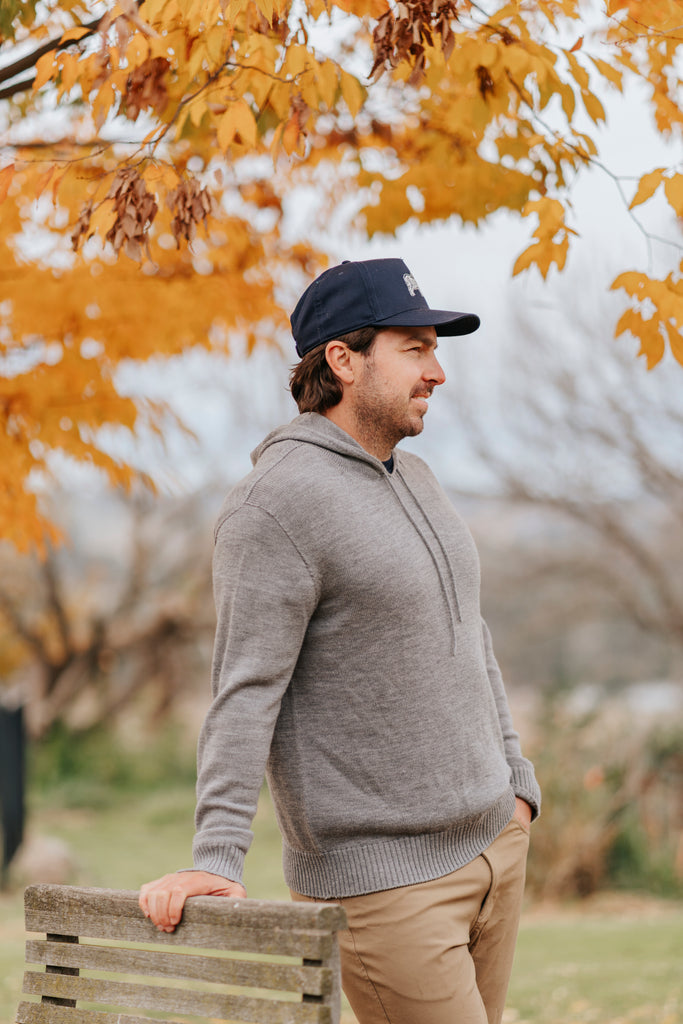 Man wearing a gray merino hoodie and navy Sir W. cap with a logo outdoors