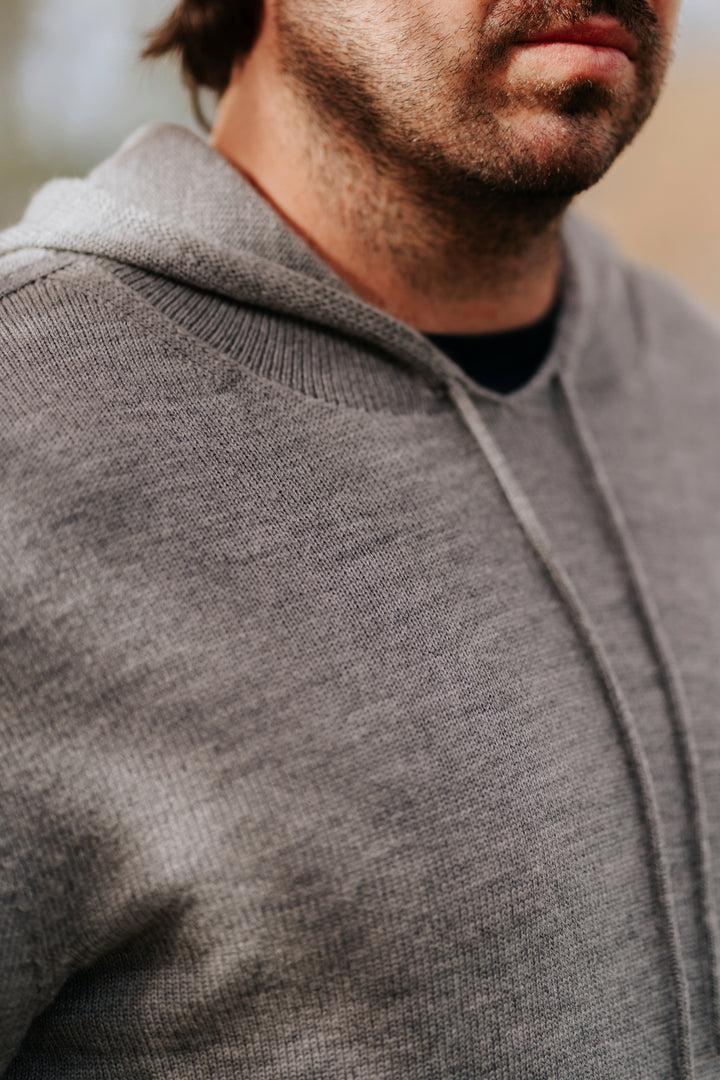 Close-up of a person wearing a gray Merino wool hoodie with a blurred background