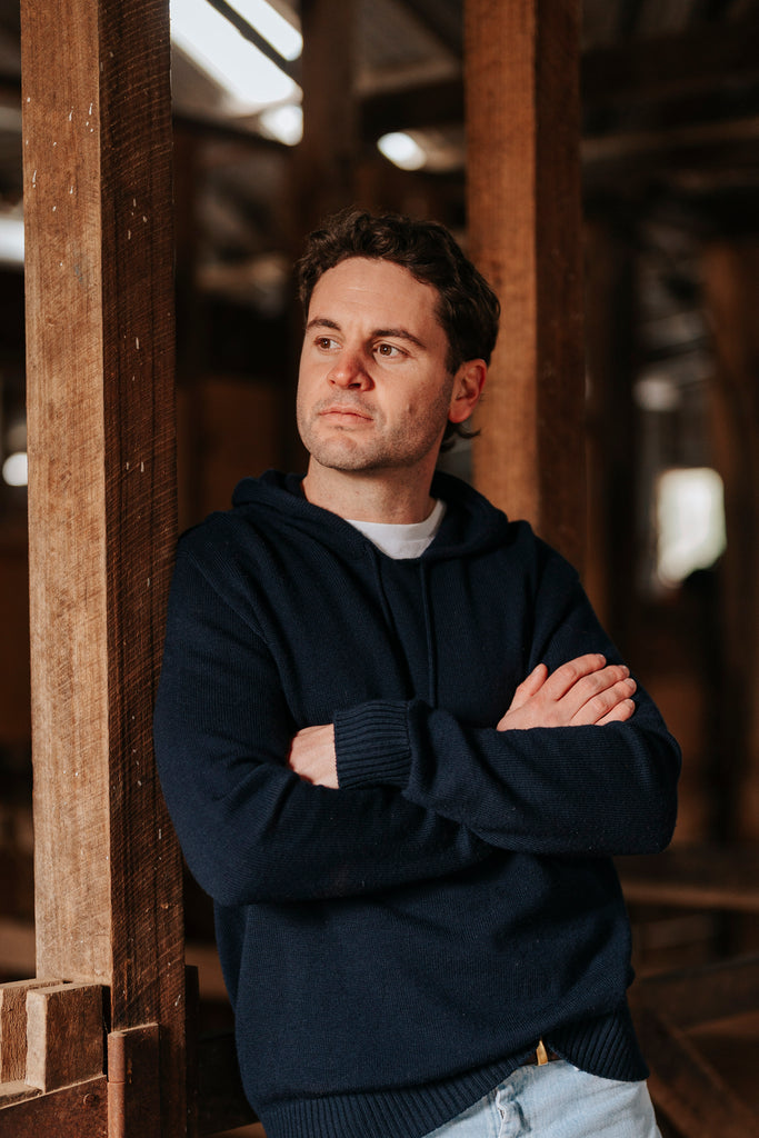 Man wearing a dark blue sweater standing in a wooden interior setting