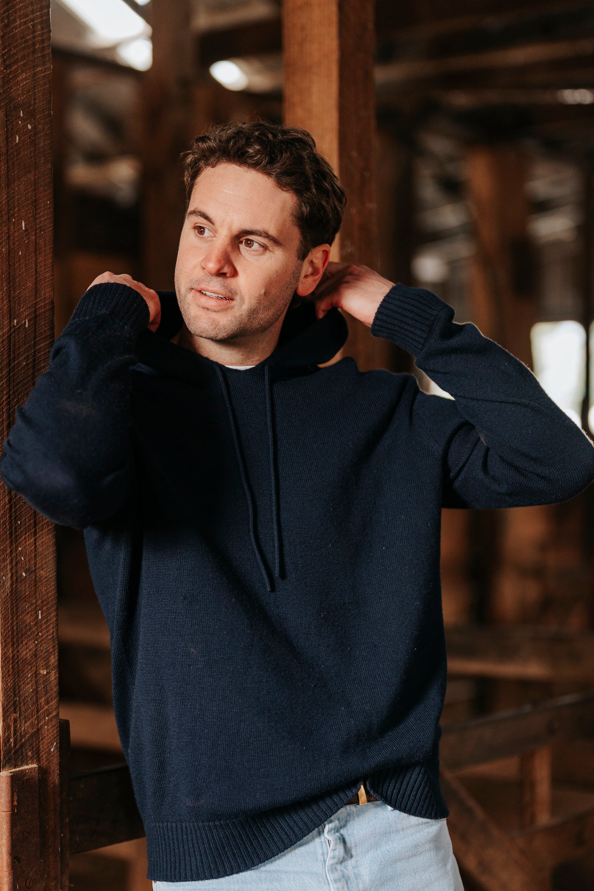 Man wearing a navy blue hoodie in an indoor setting with wooden beams.