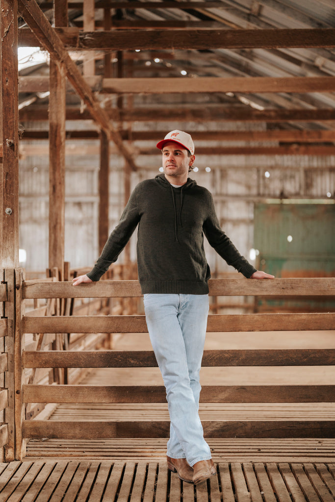 Man standing in a rustic wooden barn wearing a dark sweater and light pants.