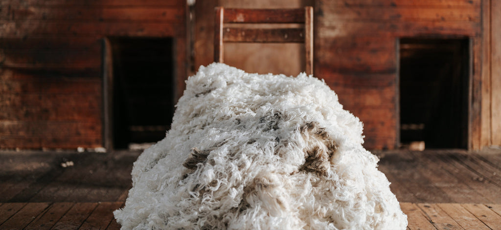 Stack of white Merino wool in front of a rustic wooden wall.