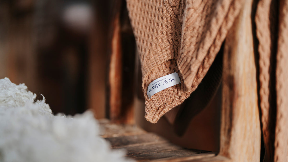 Brown textured Merino sweater with a tag on a wooden surface