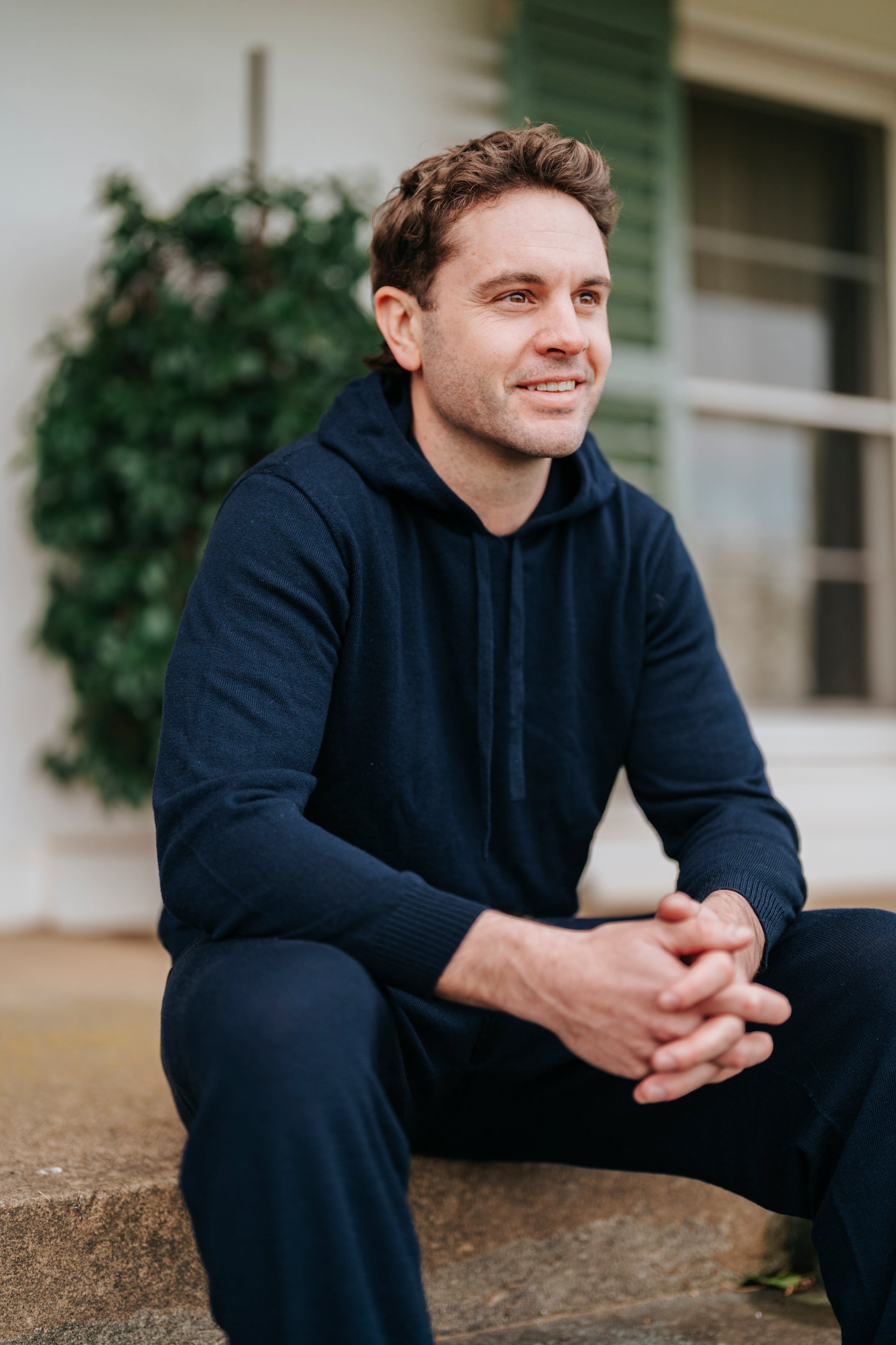 Man sitting outdoors wearing a navy blue hoodie and pants