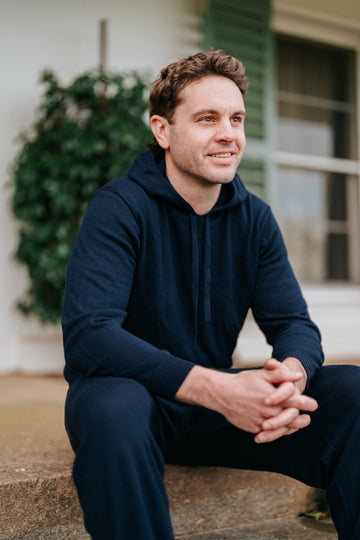 Man sitting outdoors wearing a navy blue hoodie and pants