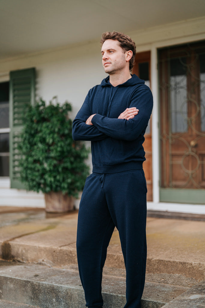 Man wearing Navy Merino Sweatpants standing on a porch with a house in the background