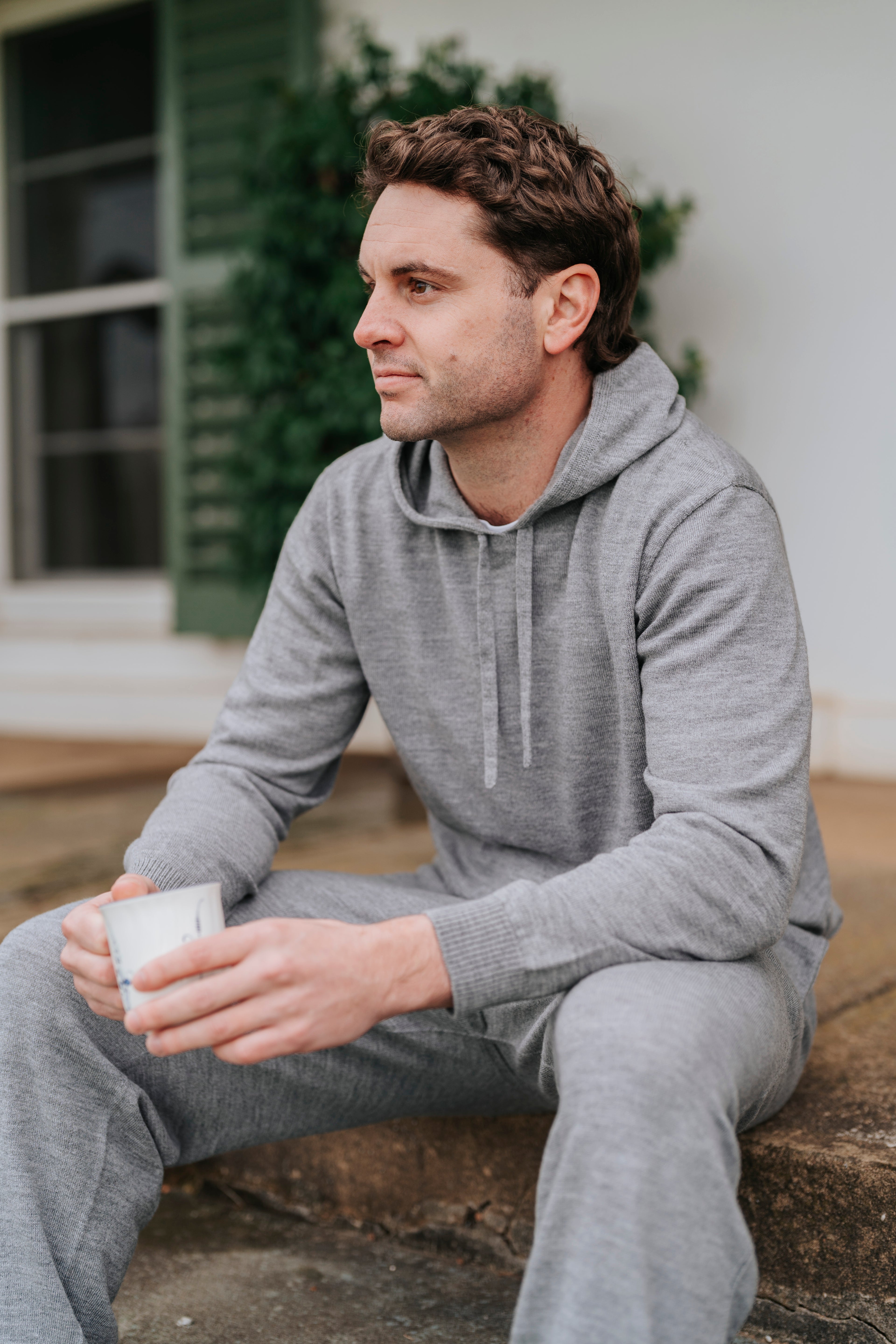Man in gray hoodie and pants holding a mug outdoors