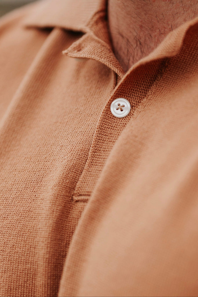 Close-up of a person wearing a brown polo shirt with a blurred background