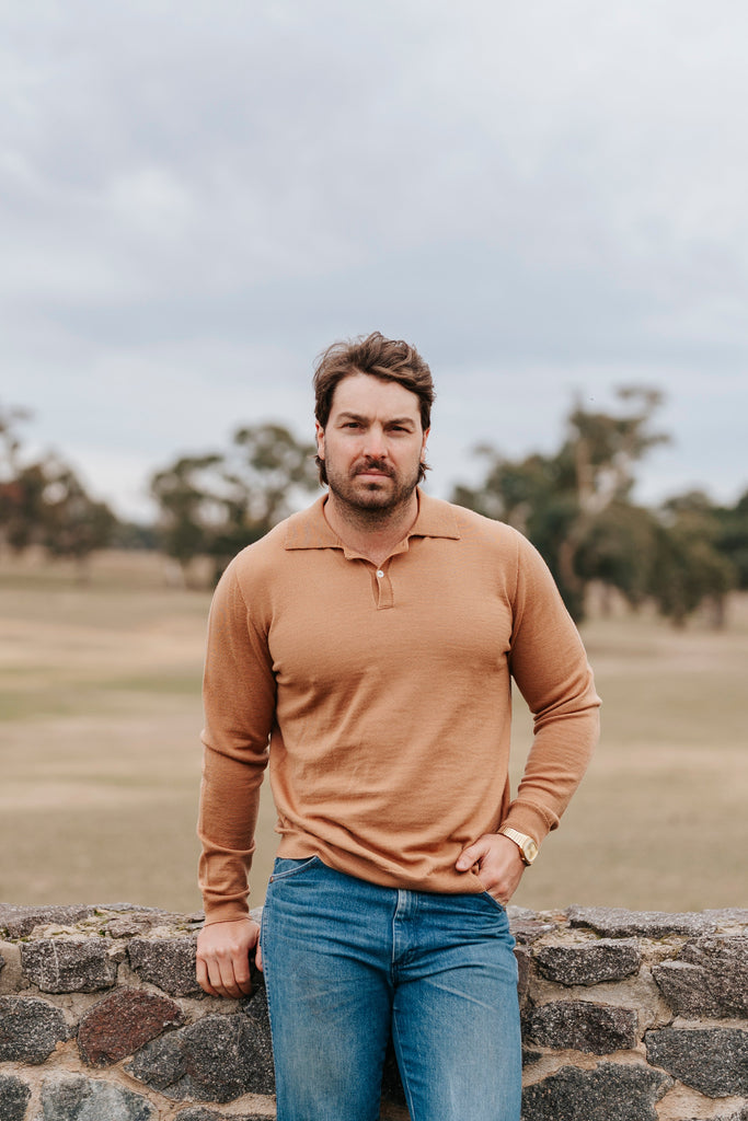 Man standing on a stone wall with a field and trees in the background
