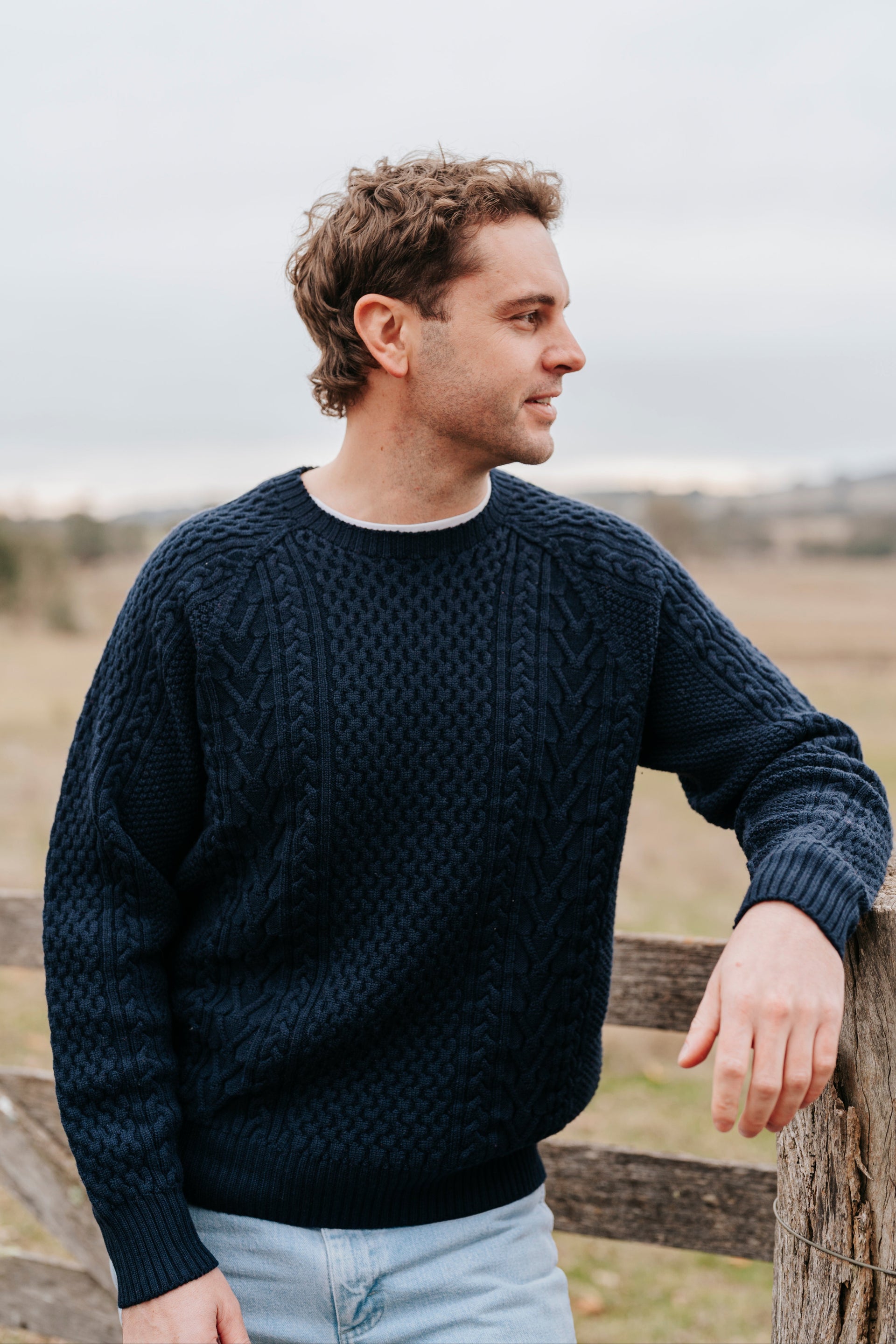 Man wearing a dark blue sweater standing outdoors with a blurred background