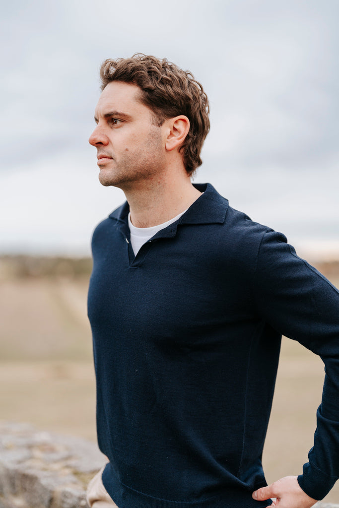 Man wearing a navy blue sweater with a blurred natural background
