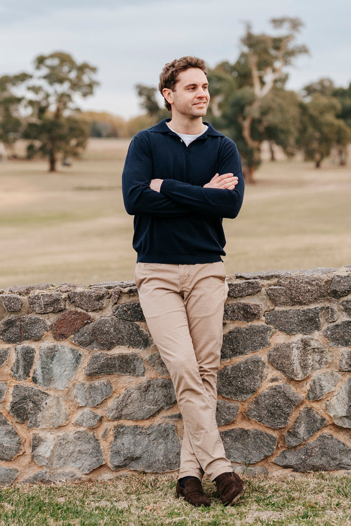 Man standing on a grassy field with trees and a stone wall in the background