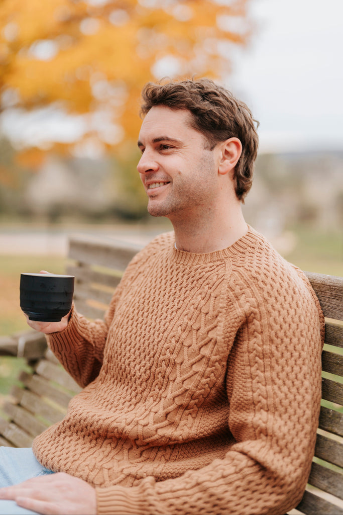 Man sitting on a bench in an autumn park holding a mug.