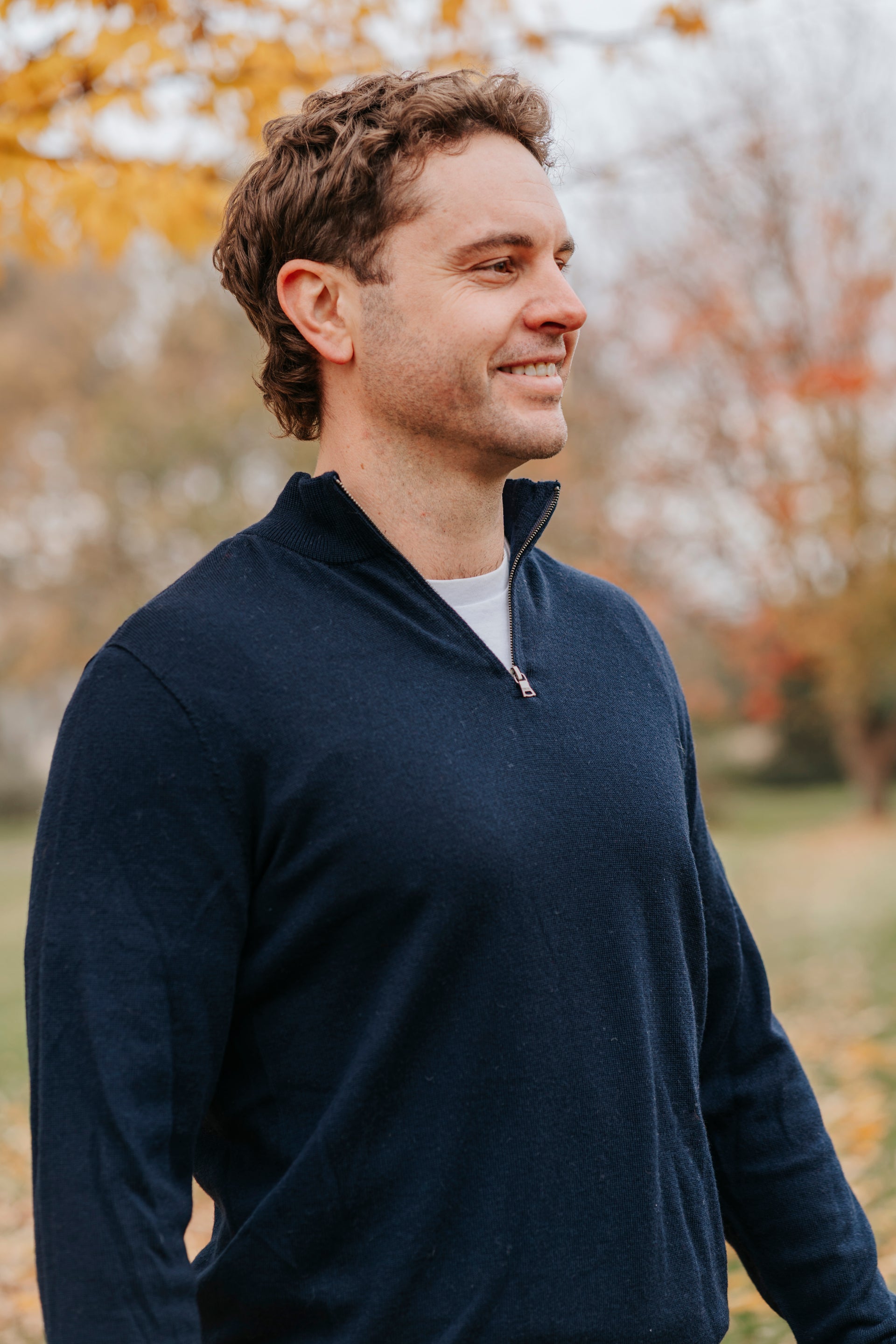 Man wearing a navy blue sweater standing outdoors with trees in the background