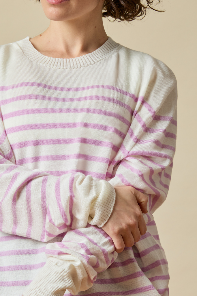 Person wearing a white Sir W. Merino sweater with pink stripes on a beige background