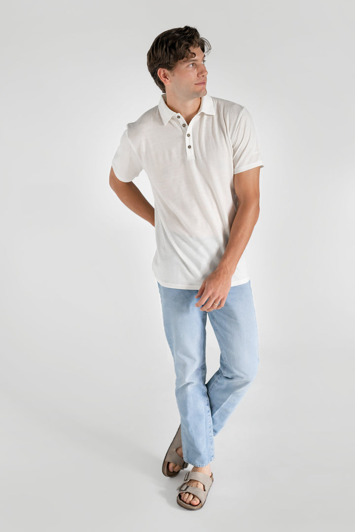 A man wearing a white merino wool polo shirt with a relaxed collar and a four-button placket, paired with light blue jeans.