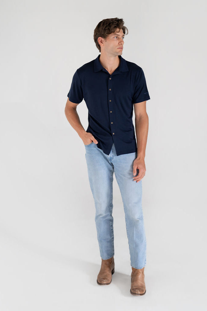 A man wearing a navy Merino button-up shirt and jeans, standing against a neutral background.