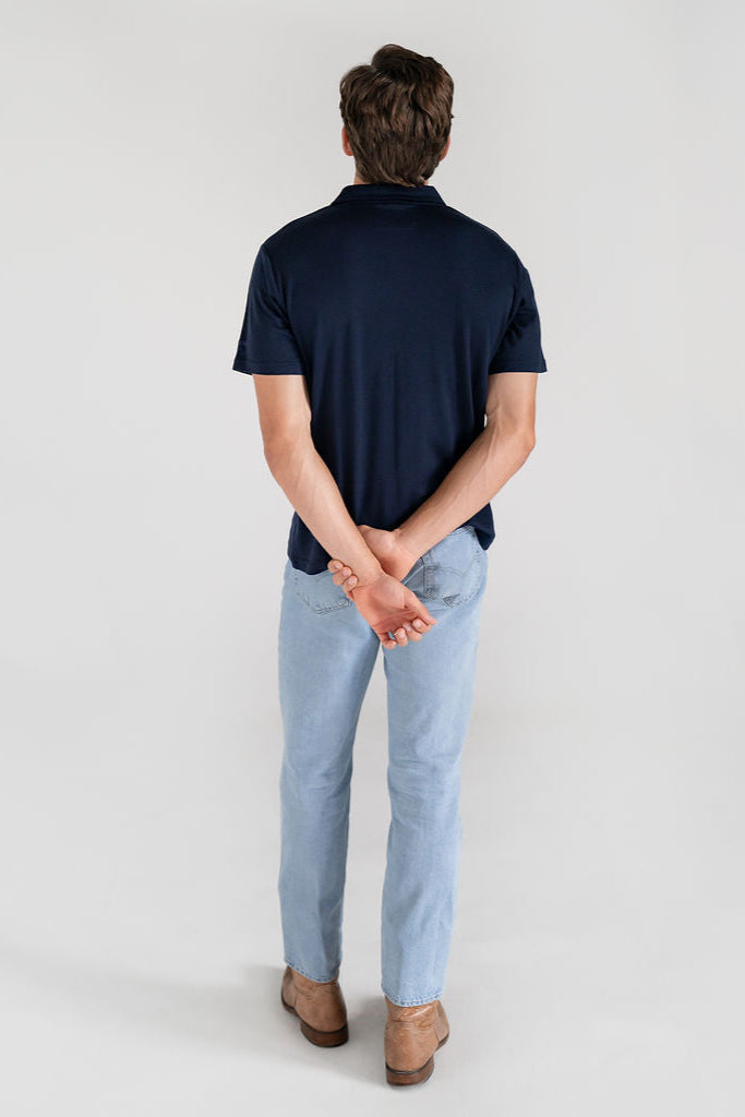 A man wearing a navy Merino button-up shirt and jeans, standing against a neutral background.
