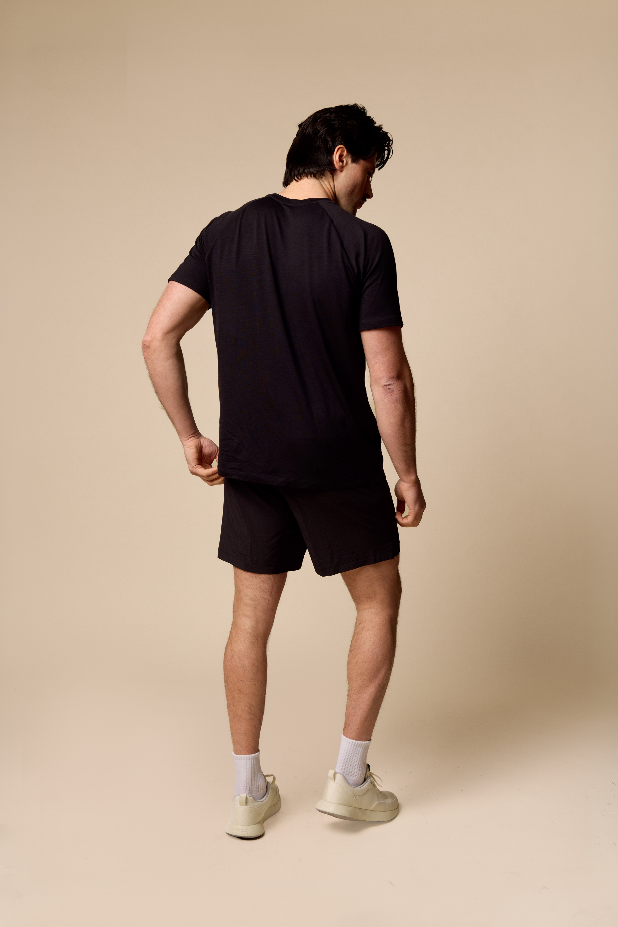 Man wearing a black Sir W. Merino t-shirt and shorts on a beige background