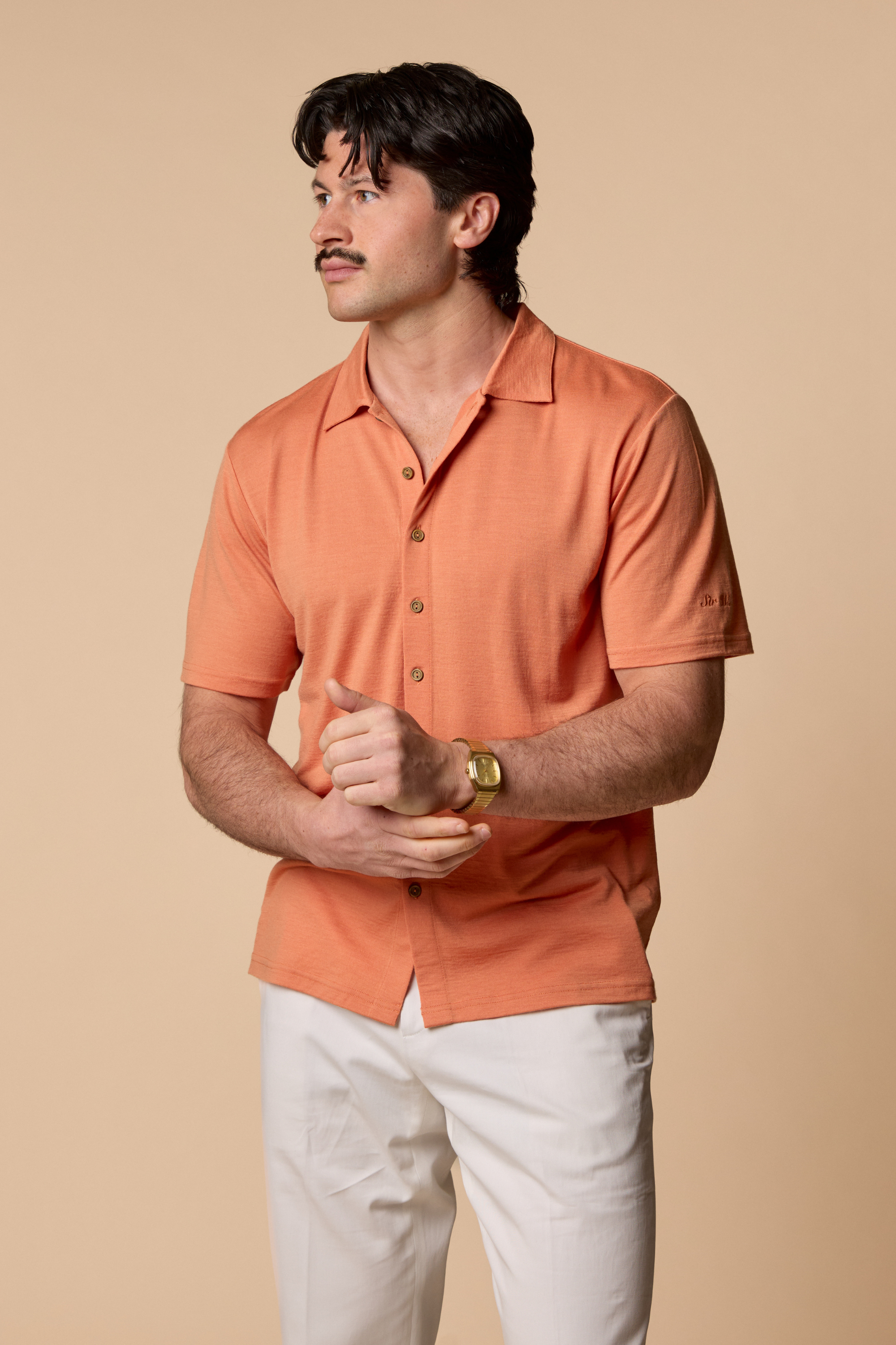 Man wearing Sir W. Merino Bruce Caramel shirt and white pants and holding watch