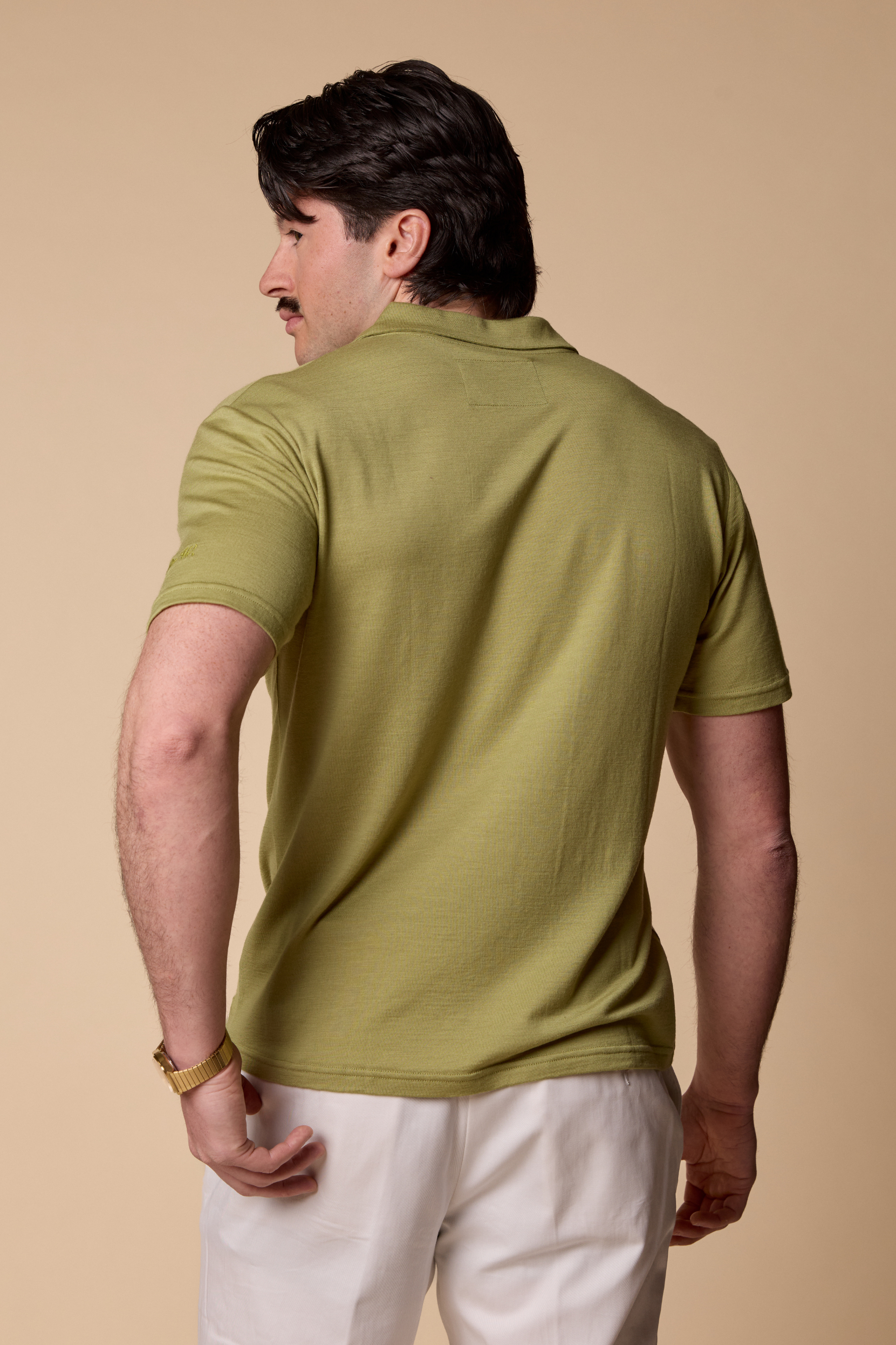 Man wearing a Sir W. Merino Bruce Olive Green shirt and white pants against a beige background