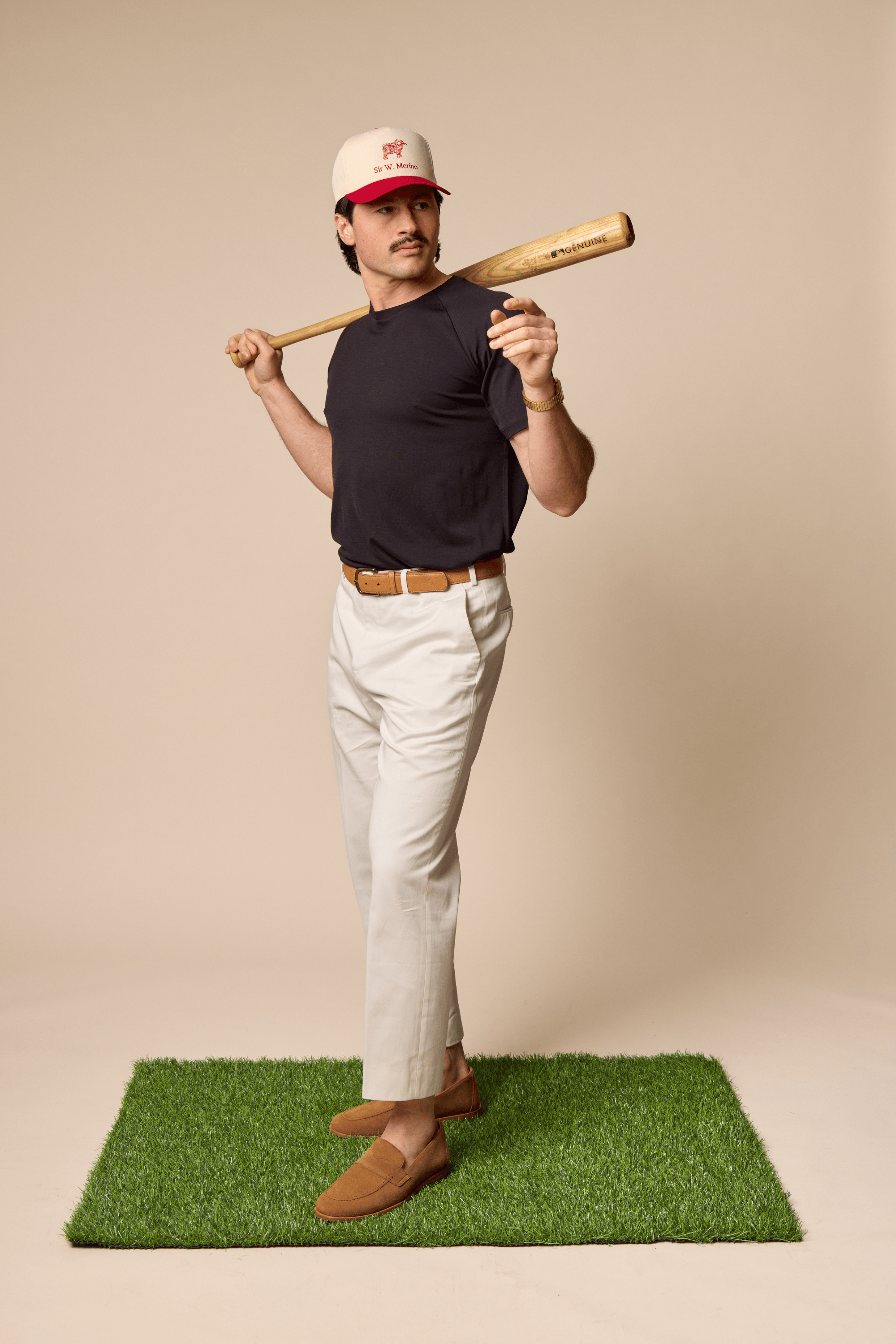 Man wearitn Sir W. Merino Cassius Black Tee and holding a baseball bat on a green mat with a beige background