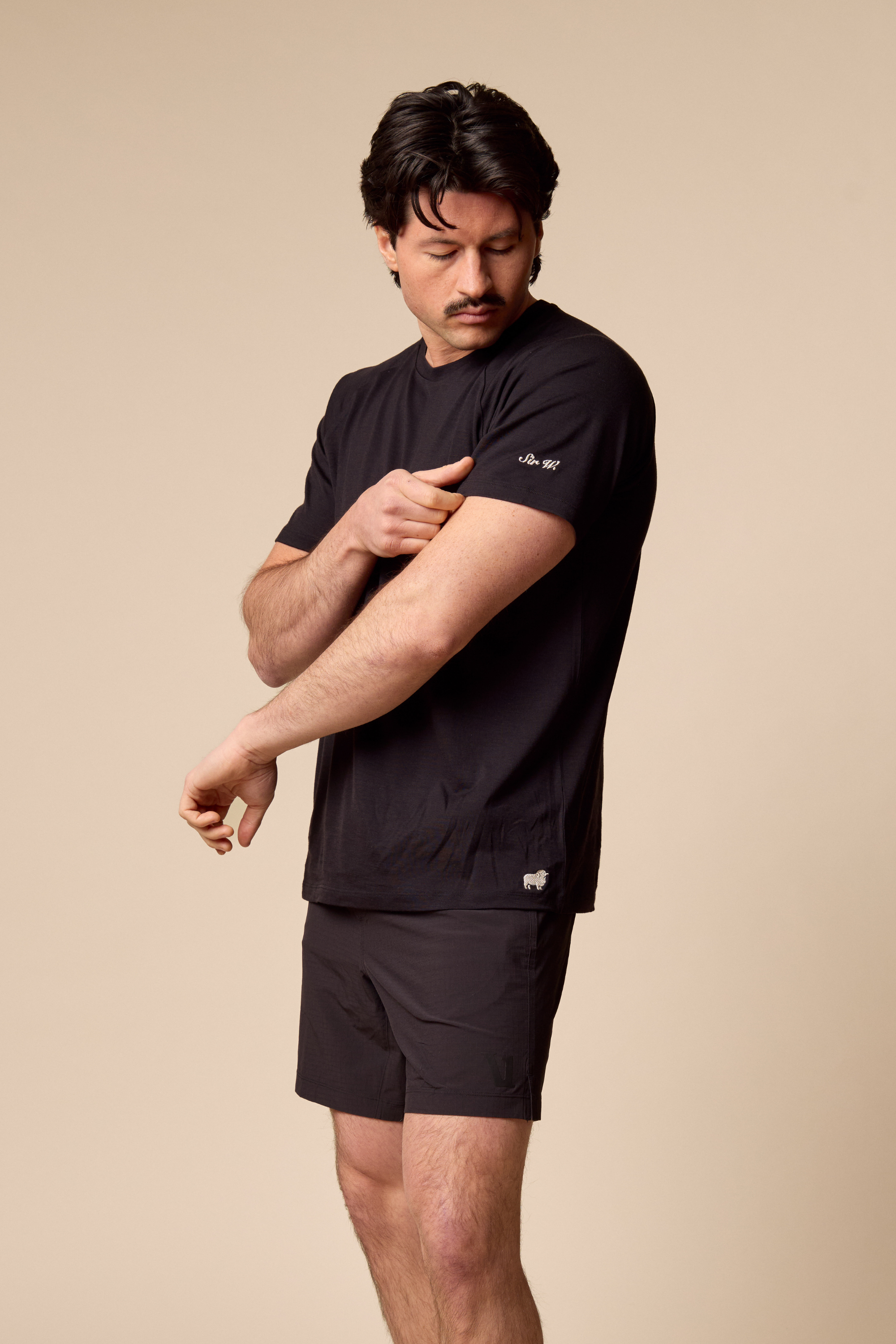 Man wearing a black Sir W. Merino Cassius t-shirt and shorts on a beige background